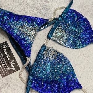 May include: A teal blue bikini top and bottom with a gradient of blue rhinestones. The bikini is decorated with silver chains.