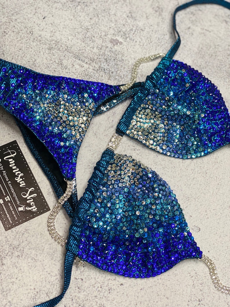 May include: A teal blue bikini top and bottom with a gradient of blue rhinestones. The bikini is decorated with silver chains.