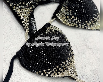May include: Black and silver bikini top with crystal embellishments. The top features a halter style strap and a low cut design. The text "Amnesia Shop by Alyona Konstantynova" is printed on the top.