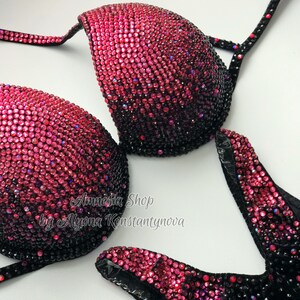 May include: A black and pink sequined bikini top with a gradient design. The top is decorated with rhinestones and has a V-neckline. The text "Amnesia Shop by Alyona Konstantynova" is printed on the top.