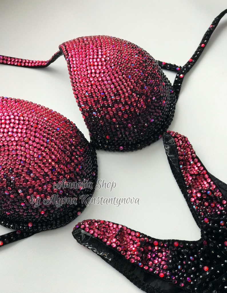 May include: A black and pink sequined bikini top with a gradient design. The top is decorated with rhinestones and has a V-neckline. The text "Amnesia Shop by Alyona Konstantynova" is printed on the top.