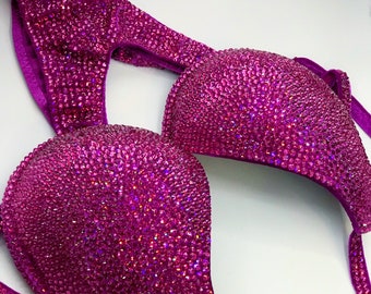 Può includere: Un top di bikini rosa con un ricamo di cristalli. Il top ha un cinturino stile halter e una scollatura profonda.