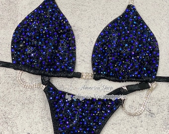 May include: Black bikini with blue and black rhinestones. The bikini top has a halter style with a chain strap. The bikini bottom has a high-cut style. The bikini is decorated with the text "Amnesia Shop by Alyona Konstantynova".