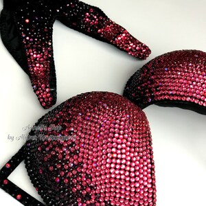 May include: A black and pink ombre bikini top with crystal embellishments. The top is made of a stretchy fabric and has a halter style strap. The top is covered in rhinestones that create a gradient effect from black to pink.