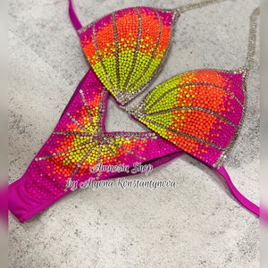 May include: A pink, yellow, and orange sequined bikini top and bottom with rhinestones. The bikini is designed with a sunburst pattern. The text "Amnesia Shop by Alyona Konstantynova" is printed on the bottom.