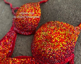 Op de afbeelding: Rode en oranje bejeweled bikini top met de tekst "Amnesia Shop by Alyona Konstantynova" op de cup.