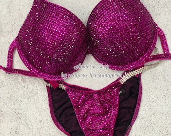 May include: A magenta-colored bikini with crystal embellishments. The bikini top has a halter style and the bottom is a high-cut style. The bikini is made of velvet and has a sheer mesh lining. The text "Amnesia Shop by Alyona Konstantynova" is printed on the bikini bottom.