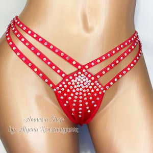 May include: Red lingerie with a criss-cross design and rhinestones. The lingerie is made of a stretchy fabric and has a low-rise cut. The text "Amnesia Shop by Alyona Konstantynova" is printed on the bottom of the garment.