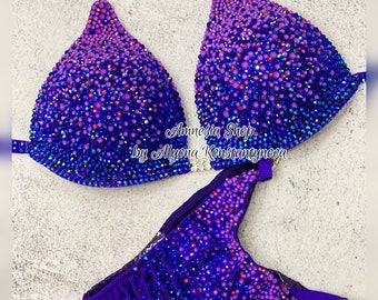May include: Purple and blue ombre bikini with crystal embellishments. The bikini top has a halter style strap and the bottom is a classic cut. The bikini is decorated with rhinestones and crystals.