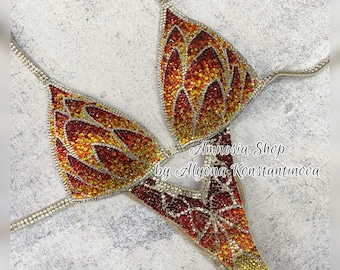 May include: A red, orange, and yellow crystal-embellished competition bikini with a geometric design. The bikini is on a white background. The text "Amnesia Shop by Alyona Konstantinova" is visible in the image.