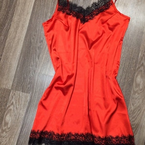 May include: A red satin slip dress with black lace trim around the neckline and hem.