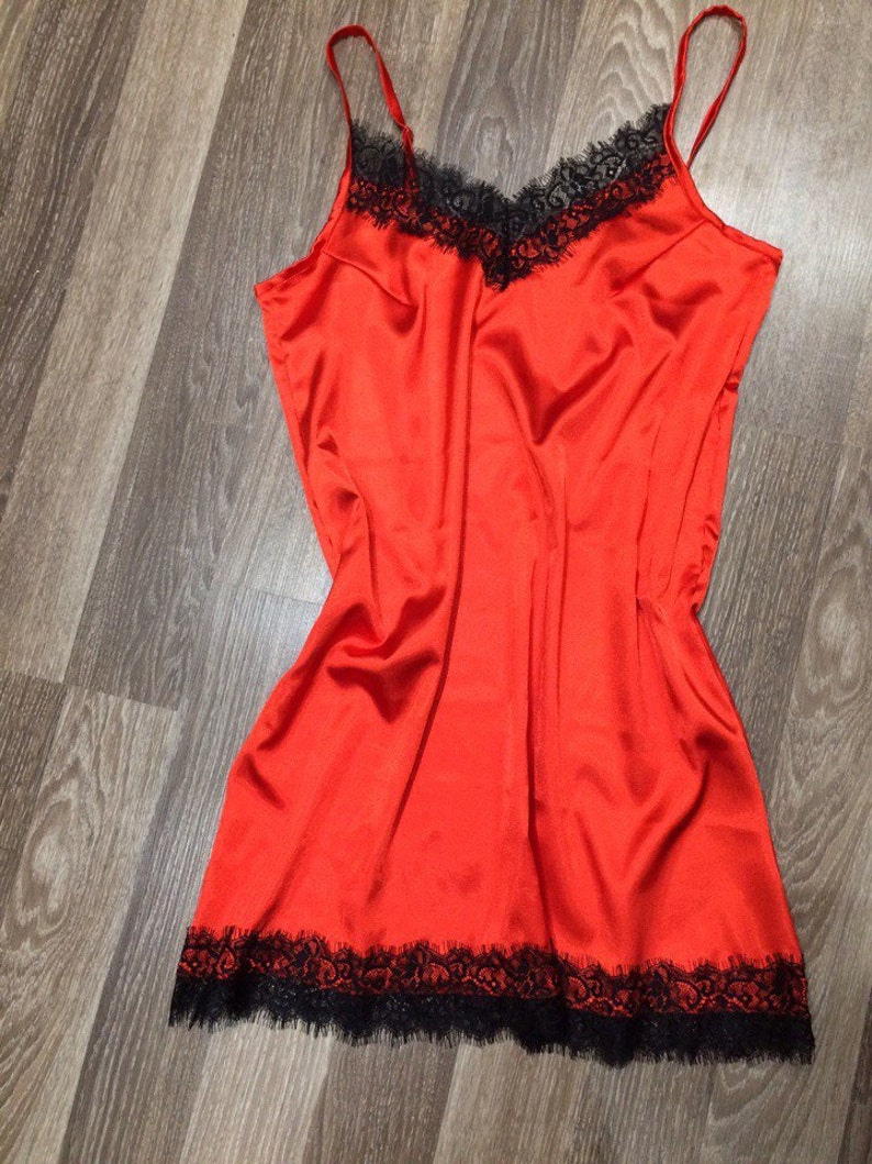 May include: A red satin slip dress with black lace trim around the neckline and hem.