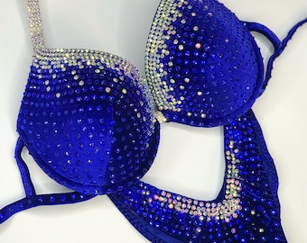 Puede incluir: Un bikini de terciopelo azul real con adornos de cristal. La parte superior tiene un escote pronunciado y tirantes ajustables. La parte inferior tiene una pierna de corte alto y una cintura baja.