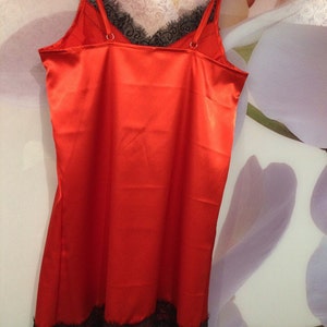 May include: A red satin slip dress with black lace trim. The dress has thin straps and a V-neckline.