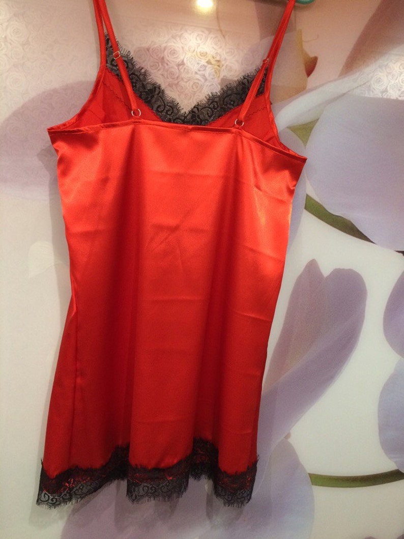 May include: A red satin slip dress with black lace trim. The dress has thin straps and a V-neckline.