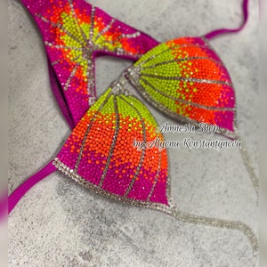 May include: A pink and green bikini top with rhinestones in a gradient pattern. The top is decorated with orange, yellow, and green rhinestones. The text "Amnesia Shop by Alyona Konstantynova" is visible on the top.