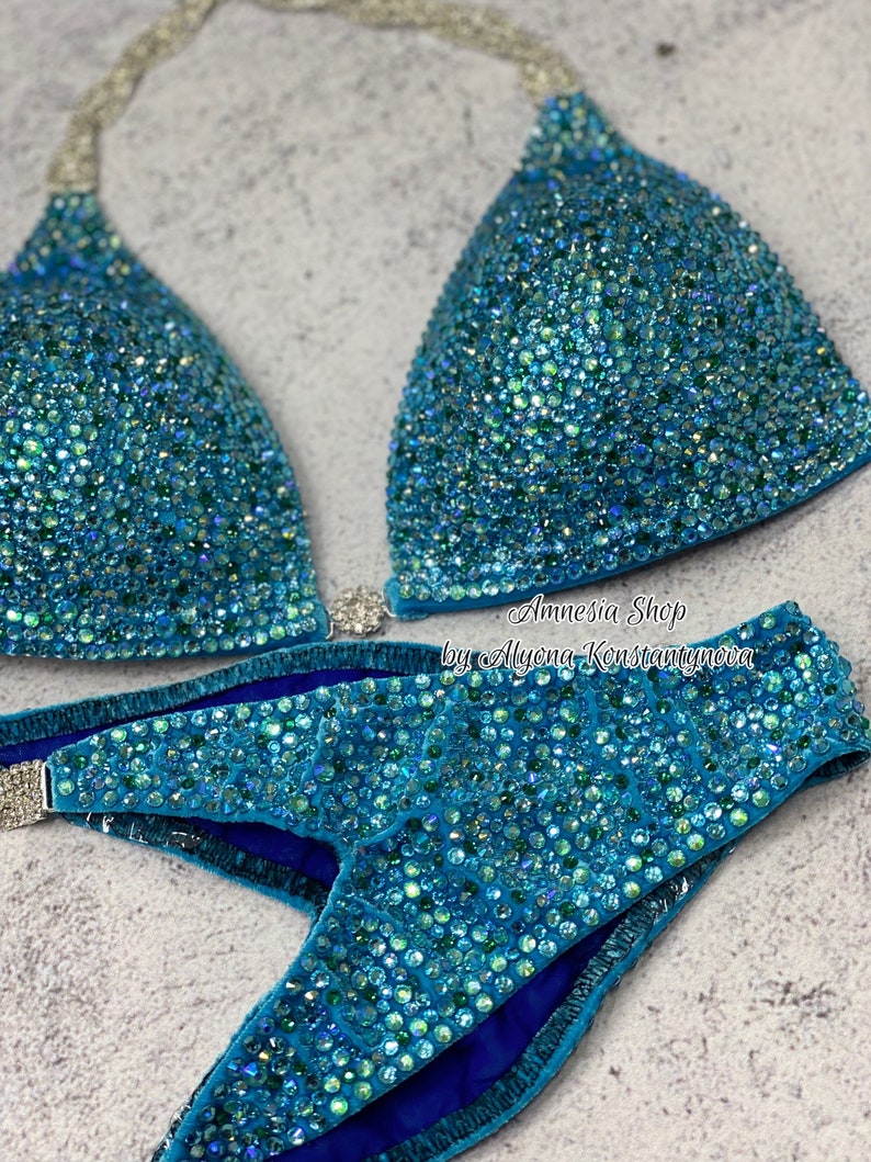 May include: A turquoise blue bikini with crystal embellishments. The bikini top has a halter style and the bottom is a high-cut style. The bikini is made of a soft, stretchy fabric and is perfect for a competition or special occasion.  Amnesia Shop by Alyona Konstantynova.