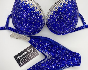 May include: A blue and silver bikini with crystal embellishments. The bikini top has a halter style strap and the bottom is a high-cut style. The bikini is decorated with a gradient of blue crystals that fade to silver. The bikini is made by Amnesia Shop.