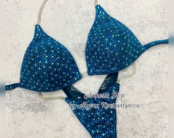 May include: Teal blue bikini with crystal embellishments. The bikini top has a halter style strap and the bottom is a high-cut style. The text "Amnesia Shop by Alyona Konstantynova" is visible in the image.