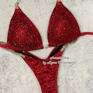 Puede incluir: Traje de competición de bikini rojo y plateado con lentejuelas. El traje tiene un top halter y una parte inferior de corte alto. El top está decorado con pedrería plateada y la parte inferior con pedrería roja. El traje está diseñado por Amnesia Shop by Allyonа Konstantynova.
