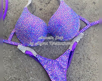 May include: Purple and silver bikini with crystal embellishments. The bikini top has a halter style strap and the bottom is a high-cut style. The bikini is labeled "Amnesia Shop by Alyona Konstantinova".
