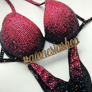 May include: A black and pink competition bikini with a gradient of rhinestones. The bikini has a V-shaped neckline and a high-cut leg. The bikini is decorated with rhinestones in a gradient from black to pink. The bikini is also decorated with a black velvet trim. The bikini is on a white background. #annesiashp