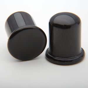 May include: Two black ear gauges, one with a flared base and the other with a flat base.