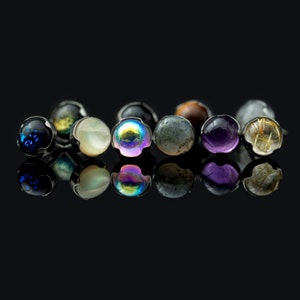 Può includere: Una fila di otto piccole perle rotonde, simili a pietre preziose, in vari colori, tra cui blu, bianco, iridescente, verde, viola e oro, incastonate in argento.