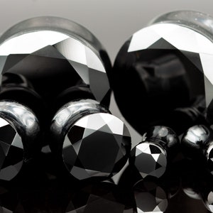 Puede incluir: Un juego de expansores de oreja de vidrio negro facetado en tres tamaños diferentes. Los expansores están hechos de vidrio negro y tienen un diseño facetado.