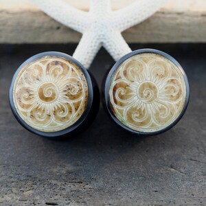 May include: A pair of black and white carved wooden ear gauges with a floral design.
