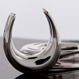 May include: Two silver ear gauges, one is a curved shape and the other is a straight shape.