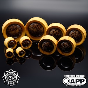 May include: A set of wooden ear gauges with a brown and yellow color scheme. The gauges have a unique design with a circular pattern on the surface.