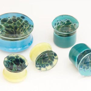 May include: Four glass ear gauges with a blue and green marbled design. The gauges are in different sizes and are made of glass.