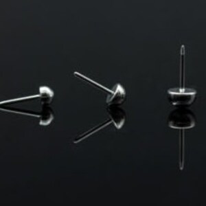 May include: Three silver tacks with round heads and sharp points. The tacks are arranged in a row on a black surface.