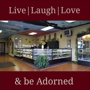 May include: The interior of a retail store featuring glass display cases filled with jewellery and accessories. The store has a wooden floor and a painted ceiling with clouds and stars. The sign above the display cases reads "Live | Laugh | Love & be Adorned".