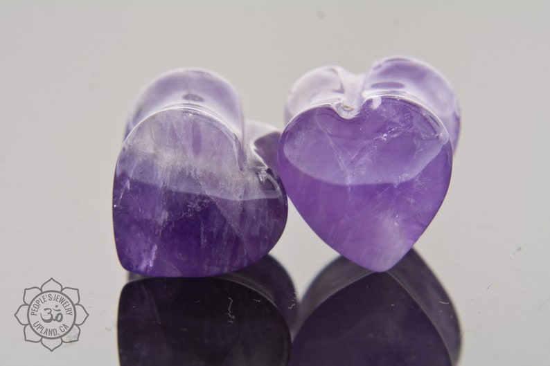 May include: Two purple amethyst heart-shaped plugs. The plugs are smooth and polished.