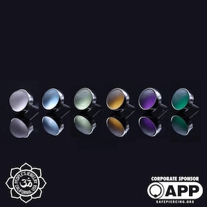 May include: Six different colored glass tops for body jewelry. The tops are round and have a smooth, shiny finish. The colors are white, blue, green, yellow, purple, and teal.