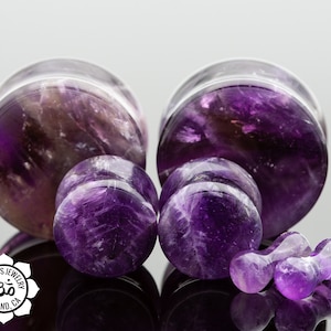 May include: Set of four amethyst stone ear gauges in various sizes. The gauges are a deep purple color with white streaks throughout. The gauges are made of natural amethyst stone.