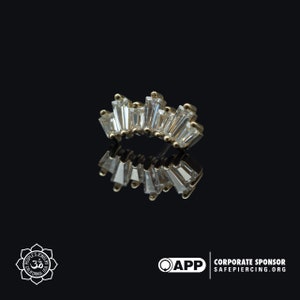 May include: A gold body jewelry piece with a row of clear baguette-shaped stones set in a curved shape.
