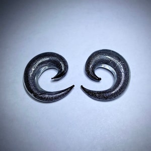 Könnte beinhalten: Ein Paar schwarze Glas-Spiral-Ohrstecker mit silbernem Glitzer, der in das Glas eingebettet ist.