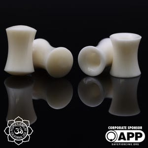 May include: Four off-white, cylindrical ear plugs are displayed against a black background. The plugs have a flared shape with a rounded base and a hollow center. The image includes the logos of People's Jewelry and APP Safe Piercing.