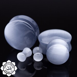 May include: Four blue and white stone ear gauges of different sizes. The gauges are made of a smooth, polished stone with a subtle shimmer. The largest gauge is on the left, and the smallest gauge is on the right.