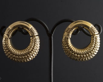 Puede incluir: Un par de dilatadores de oreja de metal dorado con diseños intrincados. Los dilatadores son circulares y tienen una superficie texturizada.