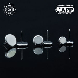 May include: Three pairs of silver stud earrings with round, flat tops. The tops are smooth and have a slightly reflective finish. The earrings are arranged in a row on a black surface.