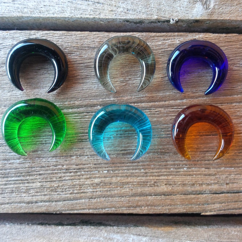 May include: Six glass crescent moon shapes in various colors, including black, gray, blue, green, turquoise, and orange. The glass is textured and has a slightly iridescent sheen.
