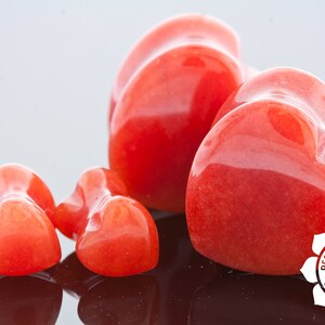 May include: Four heart-shaped red carnelian stones of varying sizes. The largest heart is in the centre of the image, with two smaller hearts to the left and one smaller heart to the right. The hearts are smooth and polished.