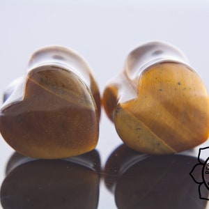 May include: Pair of heart-shaped tiger's eye stone ear gauges. The gauges are a rich brown colour with gold flecks.