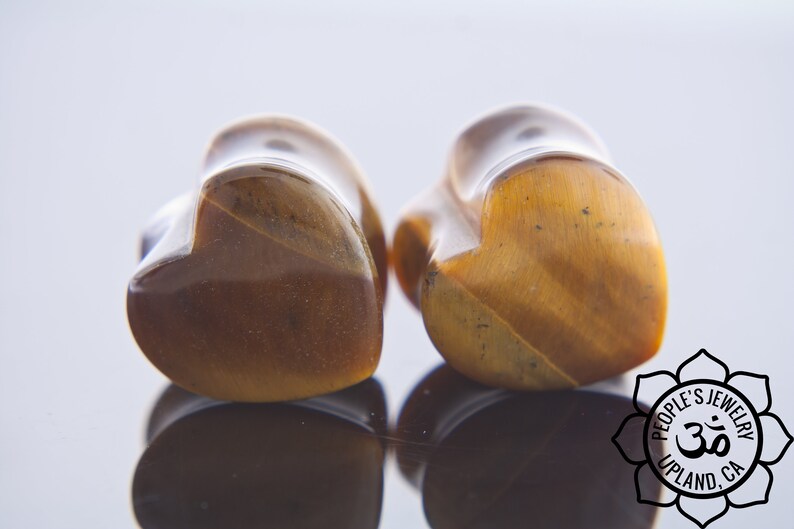 May include: Pair of heart-shaped tiger's eye stone ear gauges. The gauges are a rich brown colour with gold flecks.