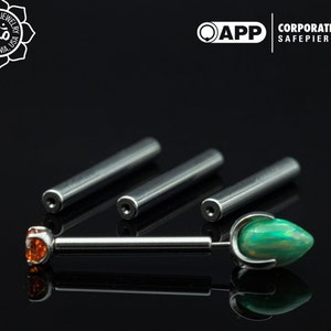 Puede incluir: Tres postes de barra de plata con un ópalo verde y una piedra preciosa naranja en un extremo. Los postes son para piercings corporales.