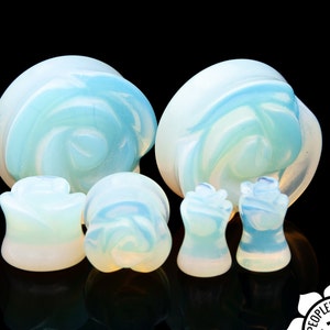 Puede incluir: Conjunto de cinco dilatadores de oreja de ópalo con diseño de rosa. Los dilatadores son de varios tamaños y son de color azul claro con remolinos blancos.